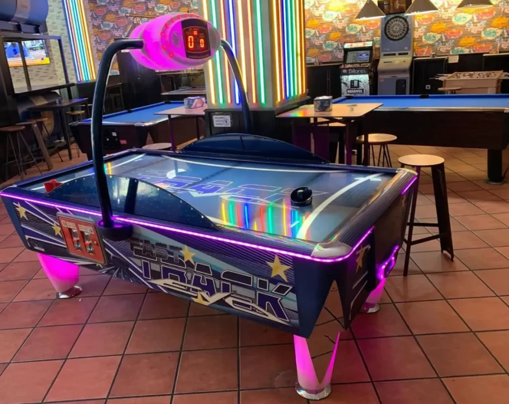 Mesa de air hockey con diseño negro y púrpura, ubicada en área interior con piso de cerámica.
