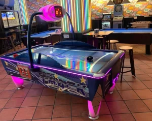 Mesa de air hockey con diseño negro y púrpura, ubicada en área interior con piso de cerámica.