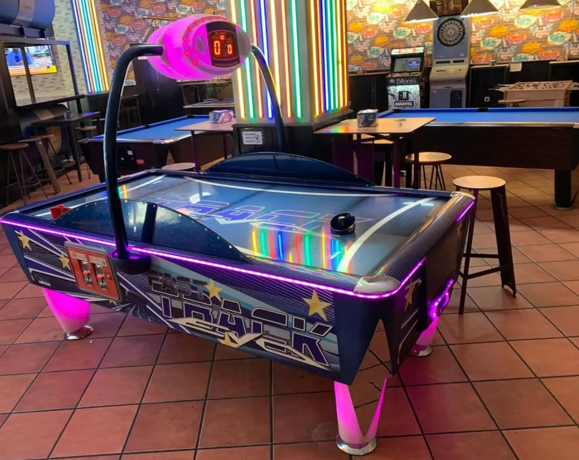 Mesa de air hockey con diseño negro y púrpura, ubicada en área interior con piso de cerámica.