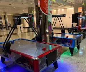 Mesa de air hockey roja y negra con marcador digital, situada en espacio interior amplio y bien iluminado.