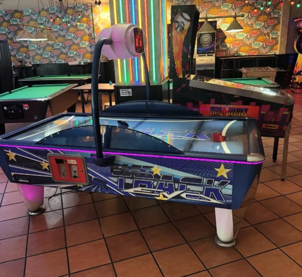 Mesa de air hockey púrpura y negra con gráficos decorativos, ubicada en espacio interior colorido y temático.