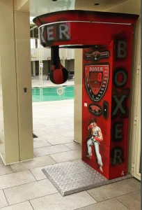 Máquina de boxeo recreativa en un área cubierta, posiblemente la entrada de un gimnasio o club.