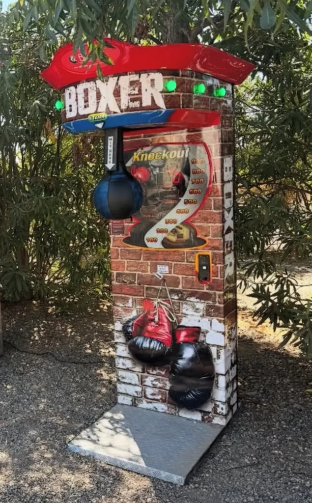 Máquina de boxeo roja sobre un pedestal de piedra, junto con guantes y sacos pequeños.