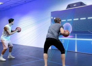 Dos jugadores utilizando un simulador interactivo MultiBall de pared. Ambos sostienen balones de baloncesto y apuntan a un objetivo proyectado en la gran pantalla. La imagen muestra líneas de detección de movimiento azules.