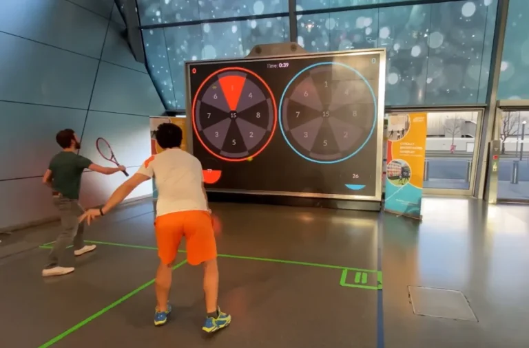 Juego de dobles en simulador interactivo de tenis con objetivo de puntuación en evento interior.