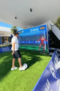 Atracción interactiva de fútbol en evento de marca en Miami, con jugador interactuando con pantalla de portero.
