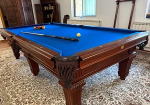 Mesa de billar de paño azul claro con maderas claras, una bola amarilla y el taco.