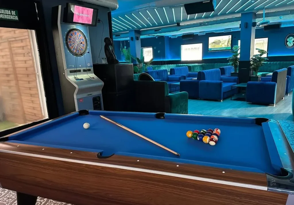 Mesa de billar de paño azul oscuro y madera oscura en un salón moderno con luces de neón.