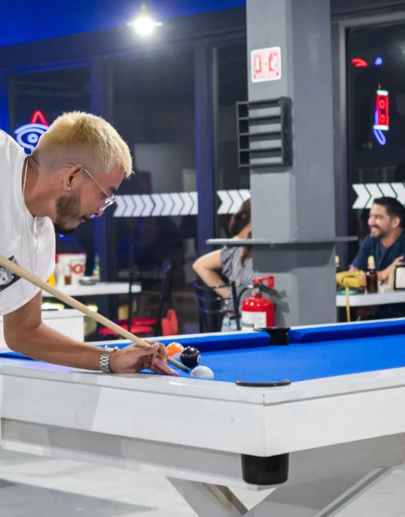 Hombre joven con camiseta azul jugando en una mesa de billar con paño azul.