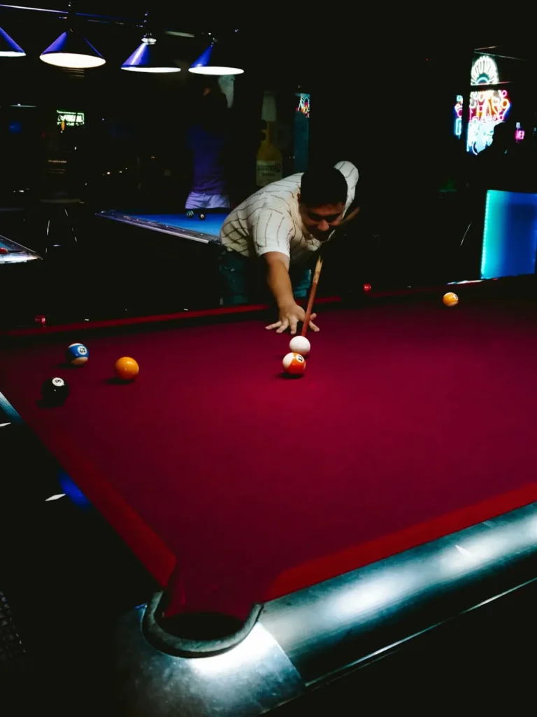 Hombre jugando billar en una mesa de paño rojo oscuro con luz focal.