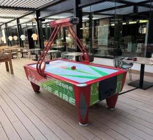 Mesa de hockey de aire (air hockey) profesional con diseño dinámico en rojo y verde, ubicada en una terraza exterior de madera para eventos privados.