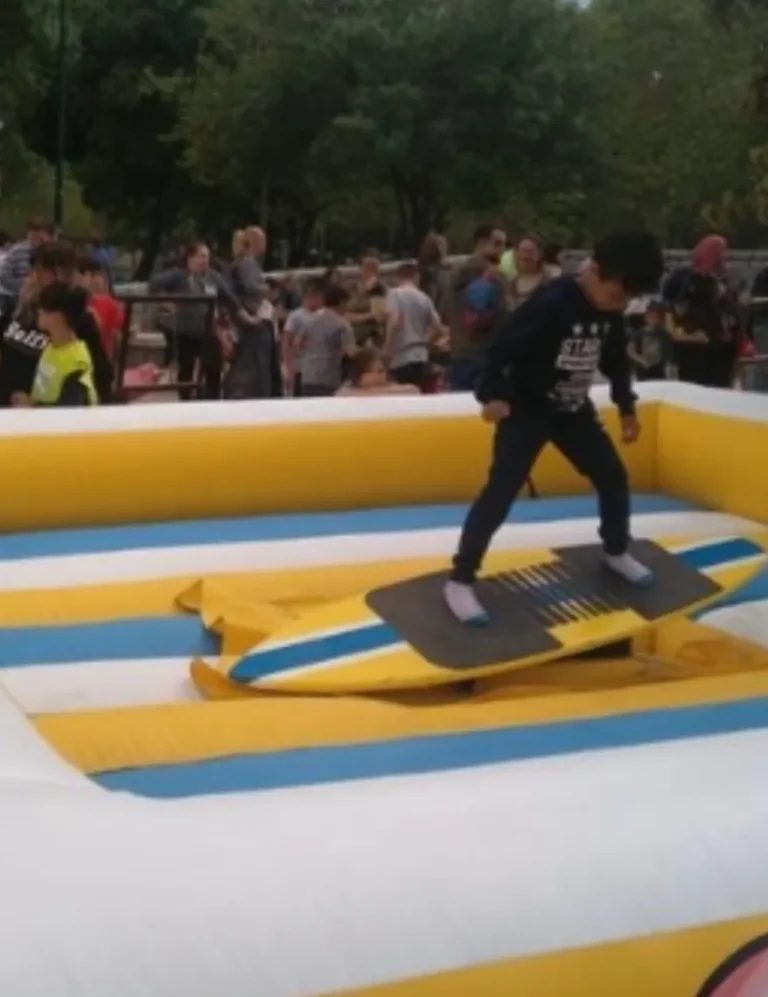 Primer plano de un niño concentrado en un juego de habilidad de equilibrio. El simulador de tabla se mueve, y el niño se apoya sobre los dedos de los pies.