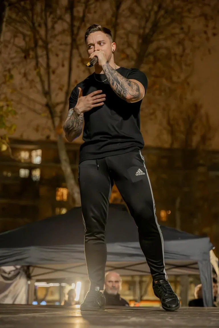 Speaker profesional en escenario exterior de noche, hablando al micrófono en un evento.