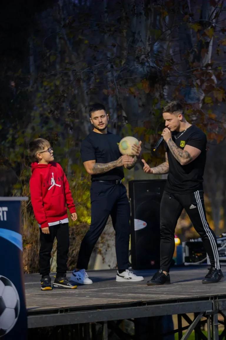 Speaker profesional interactuando con un niño y otro atleta en un escenario.