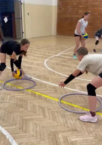 Una niña practicando técnica de recepción de voleibol en una pista interior, utilizando un aro en el suelo como guía de posicionamiento durante un entrenamiento dirigido.