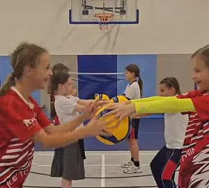 Dos niñas realizando un ejercicio de pases de dedos cara a cara, fomentando la precisión y el trabajo en equipo durante una clase de voleibol escolar.