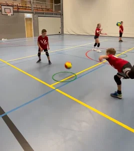 Un niño realizando un ejercicio de control de balón con un aro en una pista deportiva diáfana, mostrando las actividades adaptadas para diferentes niveles de habilidad.