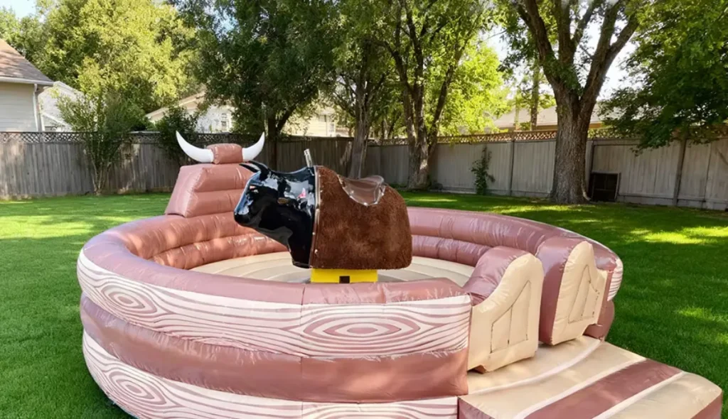 Toro mecánico inflable en un entorno de jardín o parque. La base es redonda con un diseño de tronco de madera, y el toro es negro con cuernos blancos.