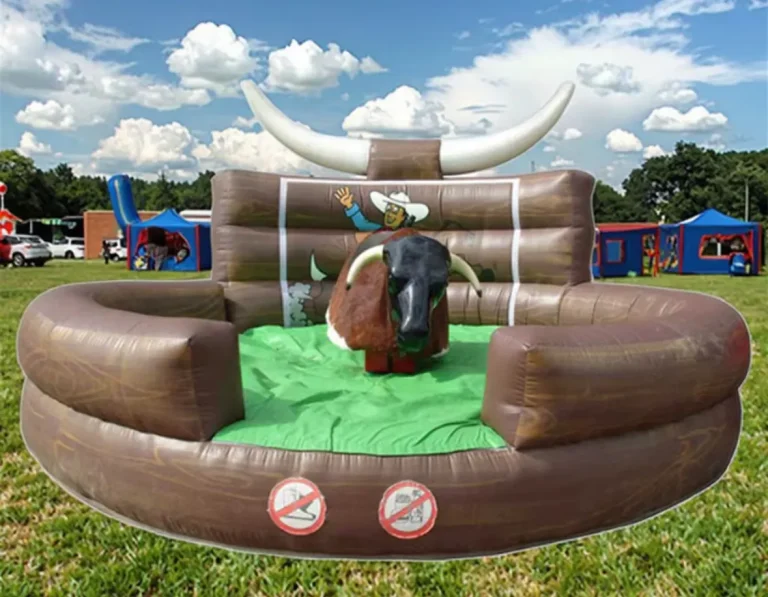 Toro mecánico marrón con silla de montar verde en una base inflable de color marrón claro, en un entorno de césped bajo un cielo azul con nubes.