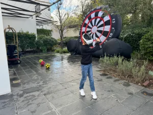Una joven con gafas de realidad virtual interactuando con un entorno digital frente a una diana de fútbol gigante en un evento al aire libre.