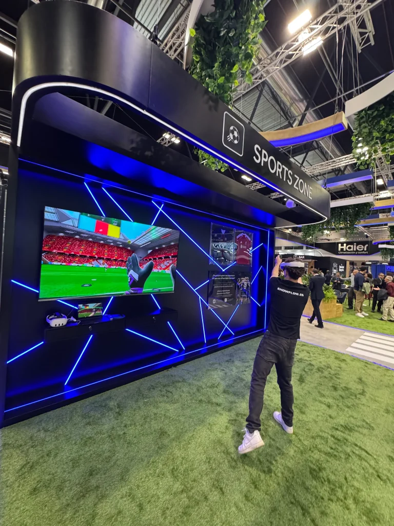 Un usuario utilizando gafas VR en un stand tecnológico de "Sports Zone", participando en una experiencia deportiva inmersiva visualizada en una pantalla LED.