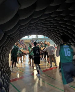 Vista desde el interior de un túnel de acceso oscuro hacia la pista polideportiva, mostrando a los jugadores entrando al campo bajo focos de luz.