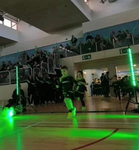 Jugador de fútbol sala realizando un regate en una pista interior ambientada con barras de luz LED verdes para una presentación espectacular.