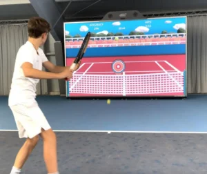 Un joven practicando tenis frente a una pantalla interactiva de gran formato que simula un estadio profesional.
